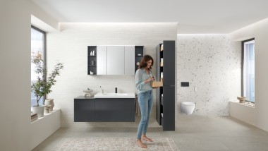 Una mujer abre un mueble alto de la serie de baño Geberit Acanto con mucho espacio de almacenamiento