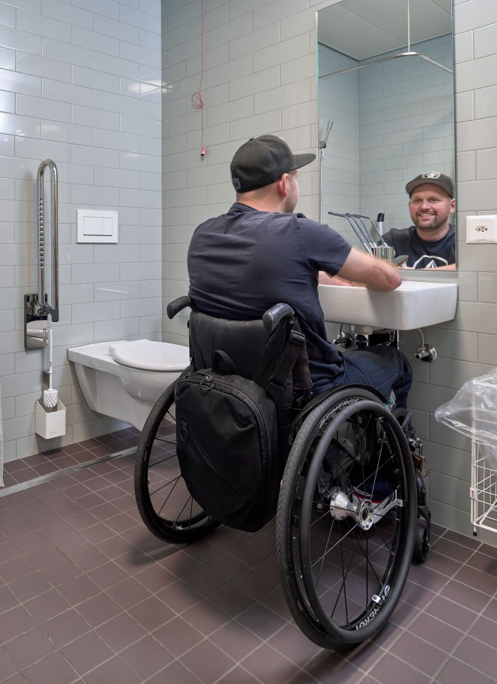 Peter Roos en silla de ruedas en el área del lavabo en un baño sin barreras (© Ben Huggler)