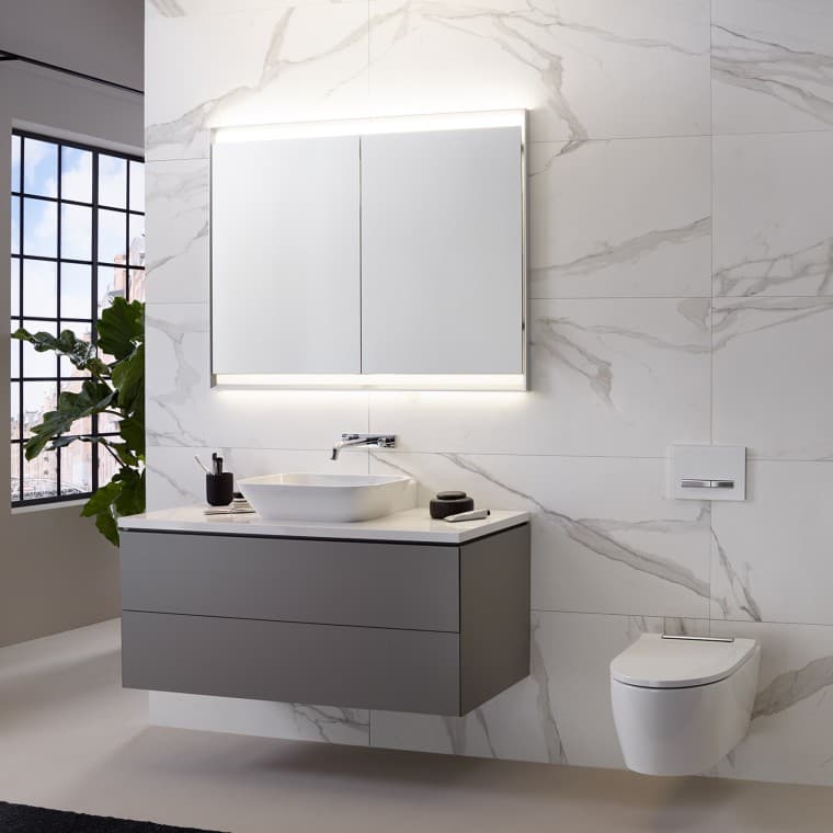 Baño con pared con baldosas con aspecto de mármol, lavabo y mueble Geberit ONE y armario con espejo con luz ComfortLight Baño con pared con baldosas con aspecto de mármol, lavabo y mueble Geberit ONE y armario con espejo con luz ComfortLight
